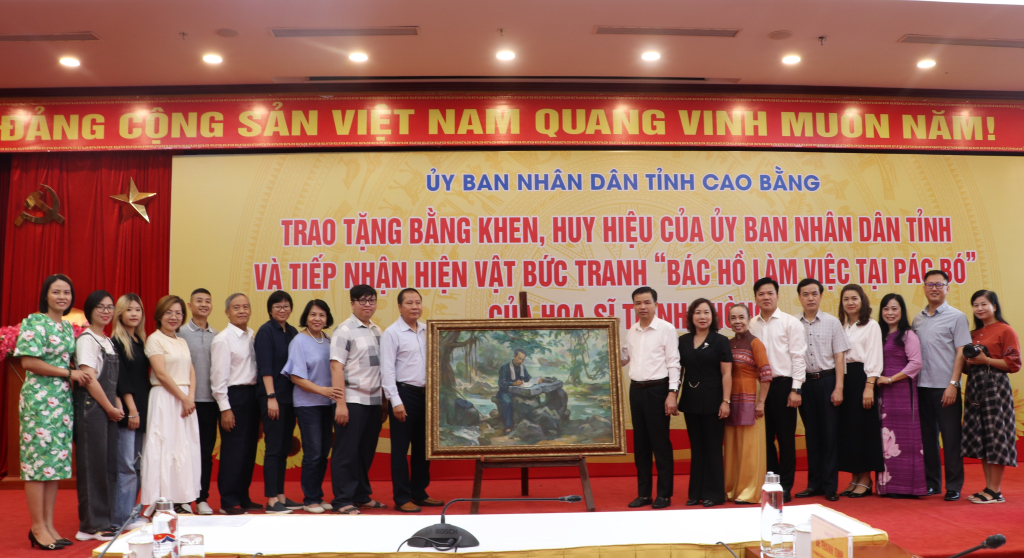 Các đồng chí lãnh đạo tỉnh chụp ảnh lưu niệm cùng gia đình họa sĩ Trịnh Phòng bên bức tranh “Bác Hồ làm việc tại Pác Bó”.